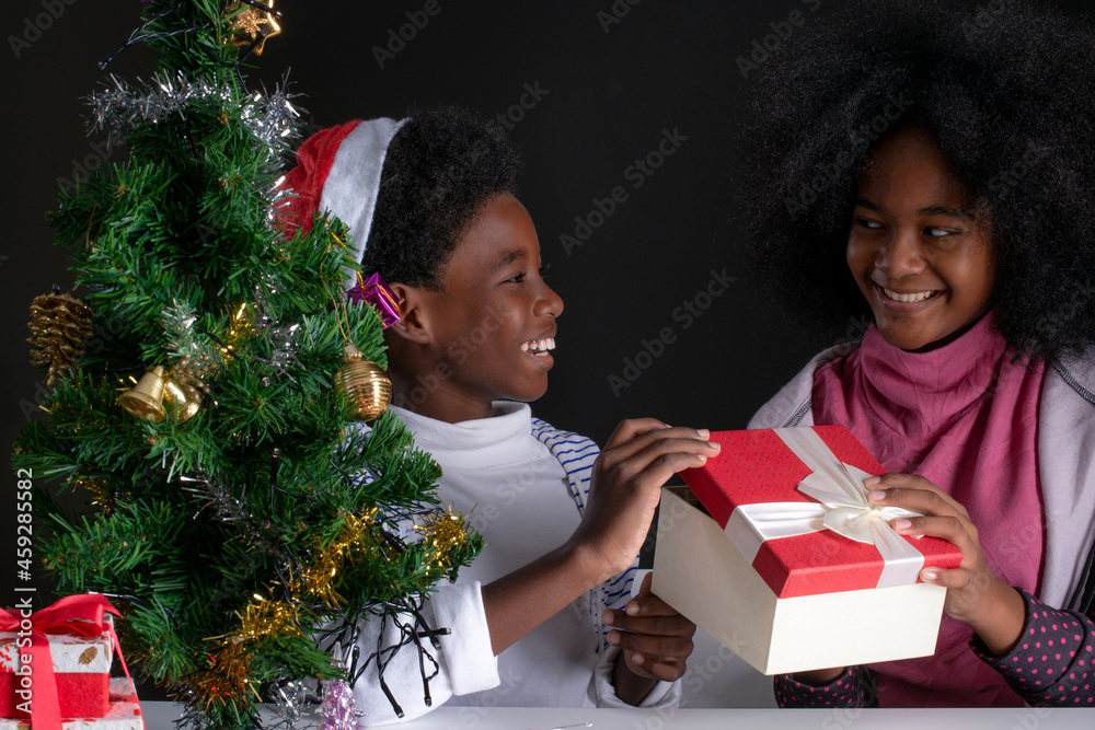 Dark-skinned brother and sister happily opened the gift box, Christmas tree on black background, New Year, Christmas celebration concept Dark-skinned brother and sister happily opened the gift box, Christmas tree on black background, New Year, Christmas celebration concept