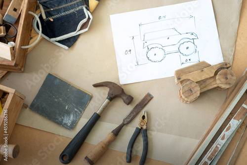 Wooden car toy and drawing design on table in the workshop, DIY wood work, wooden plank in background, concept of DIY, view from above