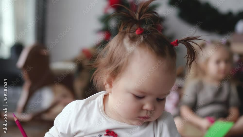 Closeup view 4k stock video portrait of cute little baby girl face with funny hair tails hairdress. Toddler baby sitting in Christmas home cozy interior, elder blurry sister in background Closeup view 4k stock video portrait of cute little baby girl face with funny hair tails hairdress. Toddler baby sitting in Christmas home cozy interior, elder blurry sister in background