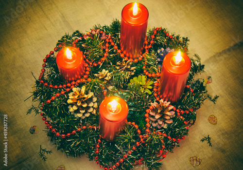 Close up of four red candles burning on advent wreath on evening. Merry Christmas, Advent crown decoration, 4th sunday, Christmas background. Advent wreath with candlelights on table in wintertime