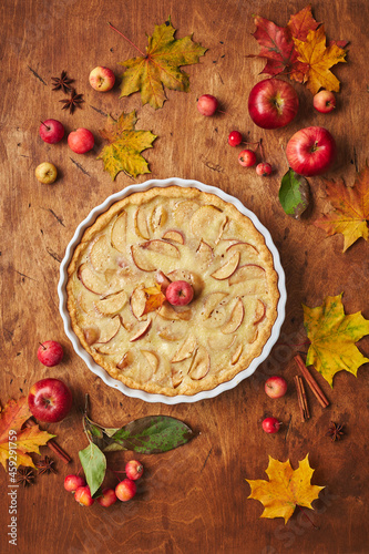 Homemade apple cake with with sour cream, red apples, Crabapples and cinnamon over wooden background, top view