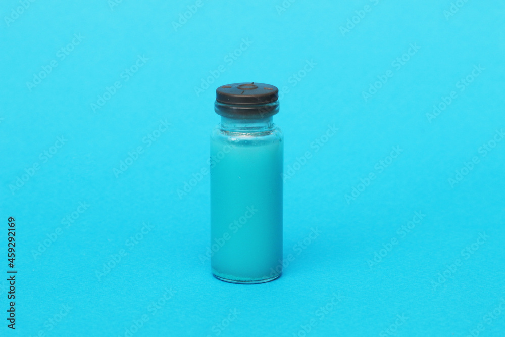 One glass clear bottle with a red vaccine medicine on a blue background. One glass clear bottle with a red vaccine medicine on a blue background.