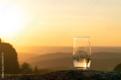 clean drinking water in a glass in the mountains, against the background of a beautiful evening sunset, copy space © Vladimir Razgulyaev