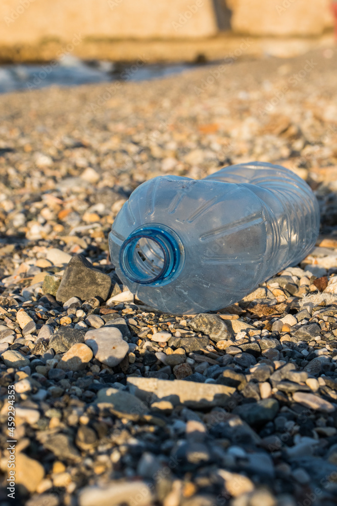 Plastic water bottle on a pebble beach. Plastic pollution. Wates on the beach. Plastic water bottle on a pebble beach. Plastic pollution. Wates on the beach.