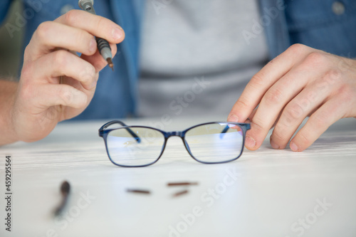 mid section of optician repairing spectacles with tool