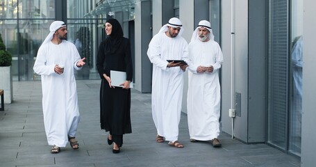 Walking arab people wearing kandura on business location. Arabic businesspeople walking on the city streets wearing dish dasha. Arabian middle eastern smiling while walking and chatting