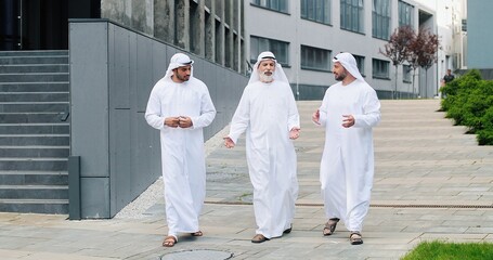 Rich and confident. Full length view of the three islamic men having conversation with each other while walking through the street. Business people concept