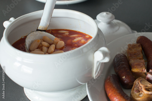 Close up of a traditional fabada home made. A ladling serving fabada from a bowl and side dish with the traditional compango, with meat, jam, blood sausages and chorizo. Asturias, Spain photo
