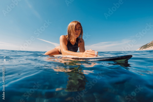 Sticker Attractive blonde surf girl on surfboard and look at camera in blue ocean