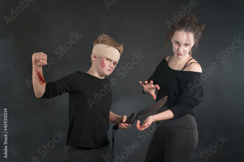 Evil-looking teenage boy mock-threatens a girl with fist and machete, both in Halloween zombie costumes