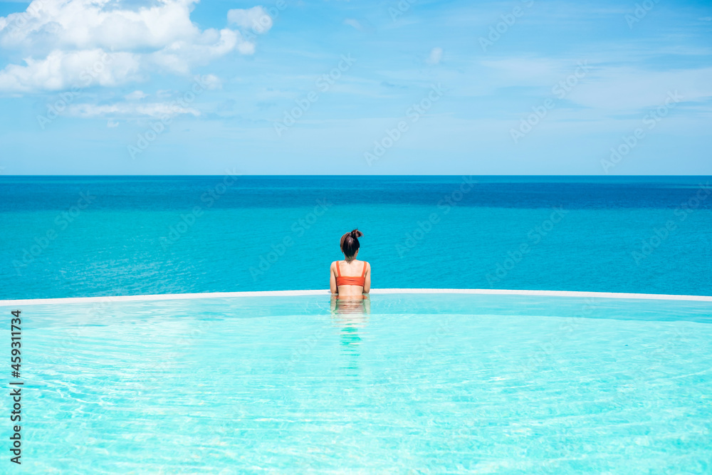 Happy woman in orange swimsuit swimming in infinity pool at luxury hotel against ocean front. young female enjoy in tropical resort. Relaxing, summer, travel, holiday, vacation and weekend concept Happy woman in orange swimsuit swimming in infinity pool at luxury hotel against ocean front. young female enjoy in tropical resort. Relaxing, summer, travel, holiday, vacation and weekend concept