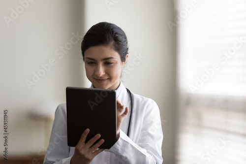 Focused young female practitioner using tablet computer. Indian doctor giving online virtual consultation, chatting to patient, making video call, virtual appointment on app. Telemedicine concept