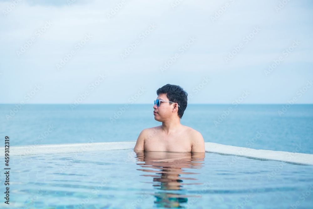 Happy man in infinity pool at luxury hotel against ocean front. young male enjoy in tropical resort. Relaxing, summer,  travel, holiday, vacation and weekend concept