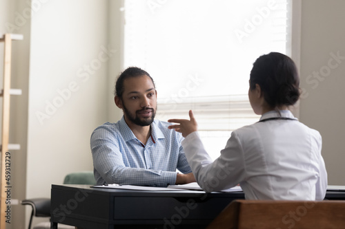 Young male patient visiting doctor, consulting young female general practitioner at home or in hospital office, talking to therapist, listening advice for treatment, therapy, recovery, healthcare