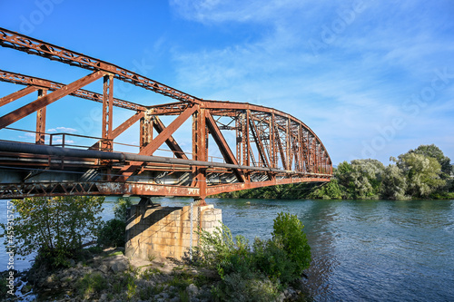 Old rusty bridge over the river. Transportation. Old metal railway bridge. Border crossing. Steel bridge across the river against blue sky.