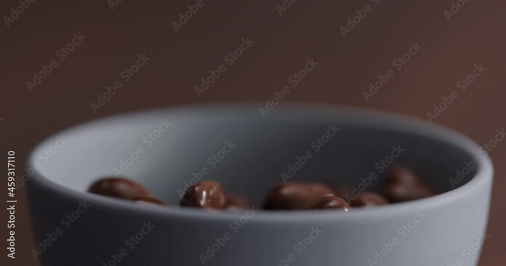 Slow motion pour chocolate covered hazelnuts in blue bowl on walnut table Slow motion pour chocolate covered hazelnuts in blue bowl on walnut table