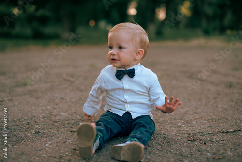 A portrait of a baby boy in a business suit walks on the pavement and shouts displeasedly.