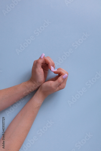 Stylish pink manicure on a blue background with place for text. Hands are folded in a heart.