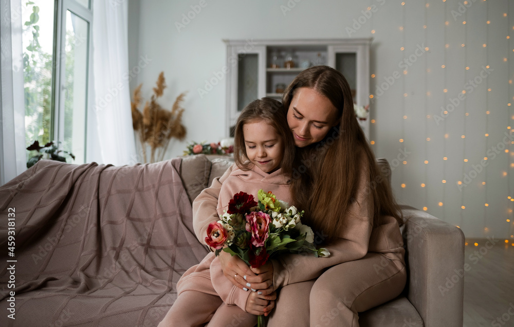 a little daughter and her mother are sitting on the sofa with a bouquet of flowers a little daughter and her mother are sitting on the sofa with a bouquet of flowers