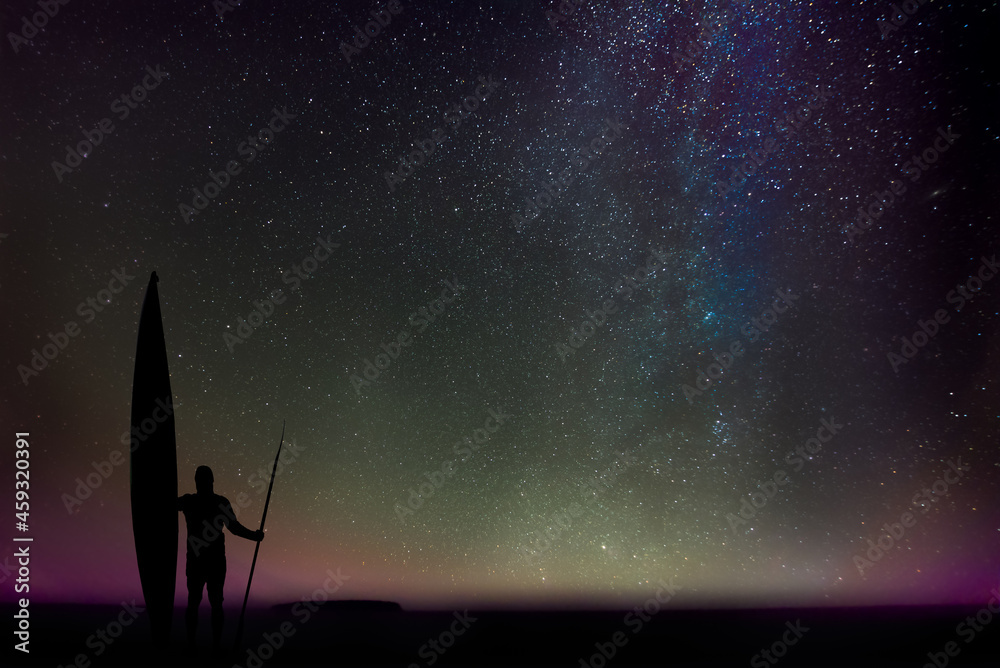 Silhouette of a man with a sea kayak and a double-bladed paddle, marvelling at the night over Lake Superior, Upper Peninsula, Michigan, with the stars of our galaxy as backdrop.