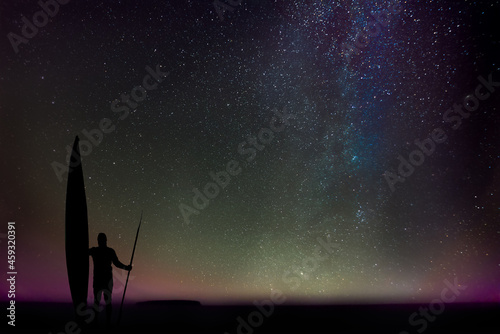 Silhouette of a man with a sea kayak and a double-bladed paddle, marvelling at the night over Lake Superior, Upper Peninsula, Michigan, with the stars of our galaxy as backdrop.