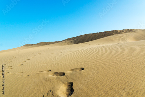 Blue sky and sand dunes with footprints.