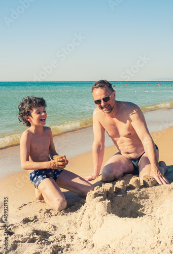 Bearded dad and little son are playing on the beach in the sand. Sea vacation on the shore on a sunny day.