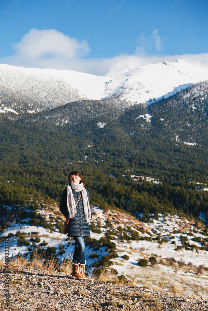 Winter portrait of young smiling caucasian woman with splendid snow-covered mountains view in background. Winter vacation.