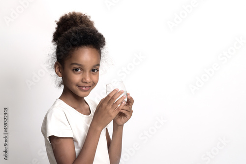 Young girl holds glass of plain drinking water. White studio background. Concept of clean, purified water, mineral balance of the body. Child with glass of water. Copy space. Eye contact.