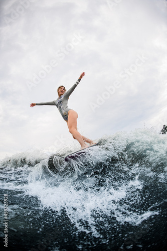 energy woman in gray wetsuit rides on wakesurf down on huge splashing river wave