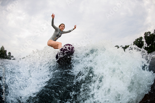 beautiful view on splashing wave and active woman on wakesurf rides down on it © fesenko