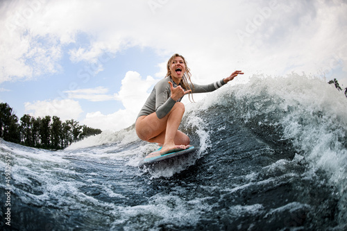 happy laughing woman rides down the wave sitting on a wakeboard and show hand gesture.