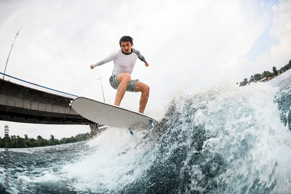 Athletic and strong man jumping on wakesurf over river waves against cloudy sky