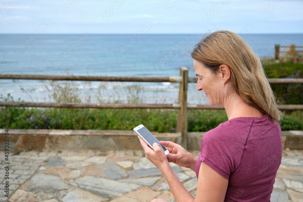 Caucasian woman watching on cell phone on the boardwalk at the beach