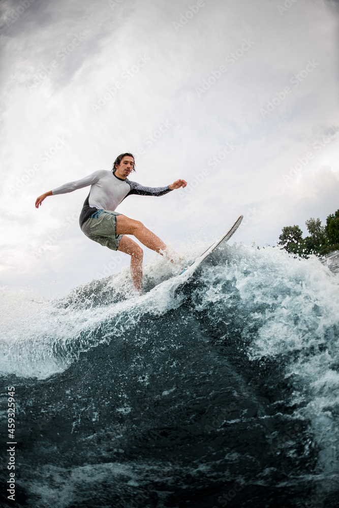 Active sportsman skilfully riding up on wave on wakesurf board.