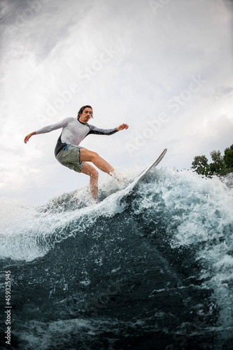 Active sportsman skilfully riding up on wave on wakesurf board.