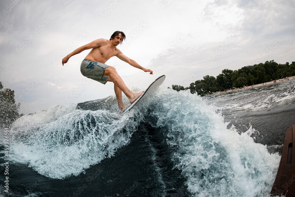 energy sportive man skilfully rides up at splashing wave on wakesurf board.