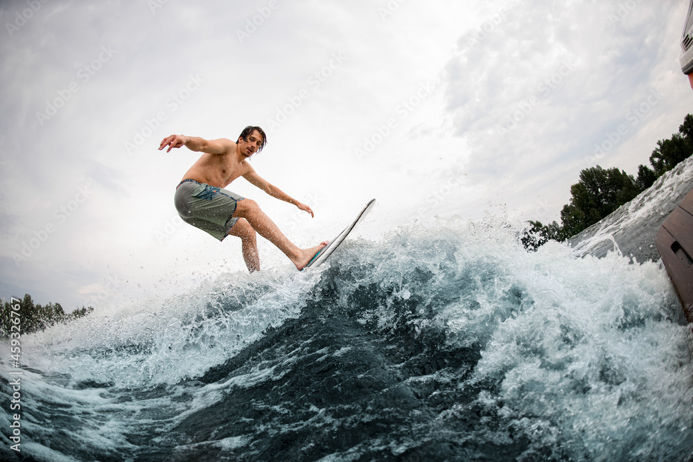 energy sportive man balancing on wakesurf board on splashing wave