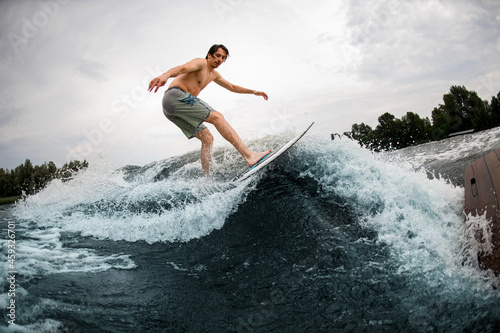 energy sportive man rides down the splashing wave on wakesurf board.