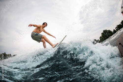 energy sportive man balancing on wakesurf board on splashing wave