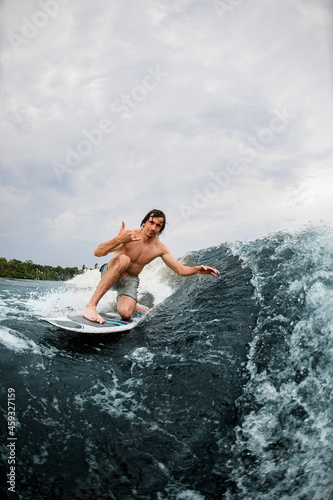 Active man show hand gesture riding the wave on surf style wakeboard