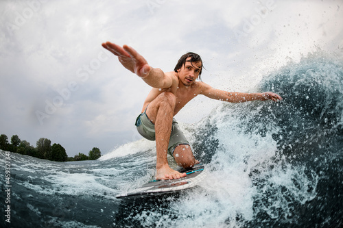 Close-up of wet man balancing on surf style wakeboard and touching the wave with one hand.