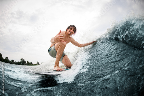 man show hand gesture riding on surf style wakeboard and touching the wave with one hand