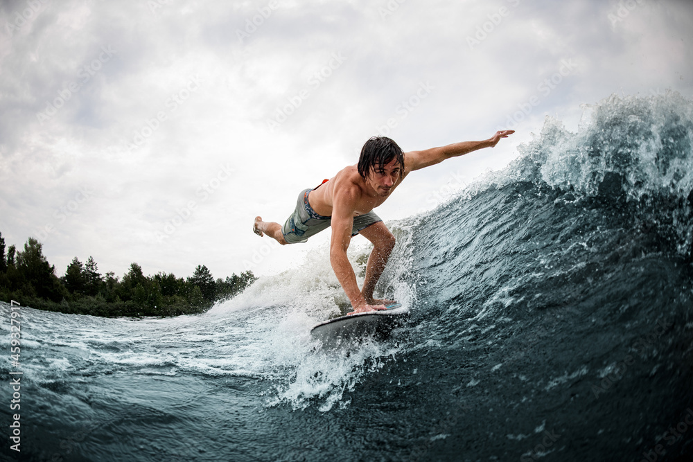 man make trick balancing on wake surf board on wave with stretching his leg and hand