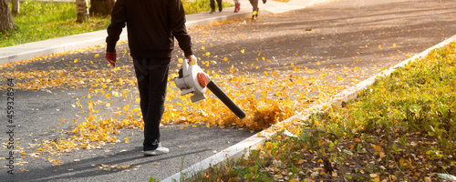 A man, a utility worker, removes leaves from the road with a special device. photo