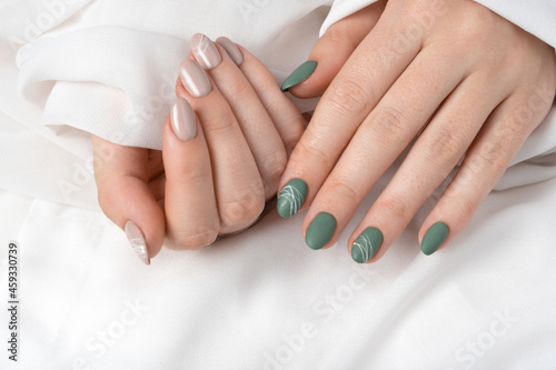 Hands of a young woman with green olive matte nails and beige glossy nails on light gray background