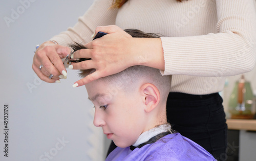 Cheerful Caucasian boy getting hairstyle in barbershop.