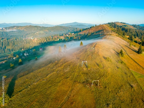 Fototapeta Naklejka Na Ścianę i Meble -  Fog in the mountains in the early morning spreads along the slopes of the mountains. Ukrainian Carpathians in the morning in the haze. Aerial drone view.
