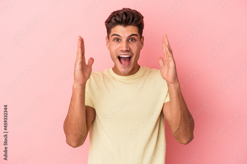 Naklejka premium Young caucasian man isolated on pink background celebrating a victory or success, he is surprised and shocked.