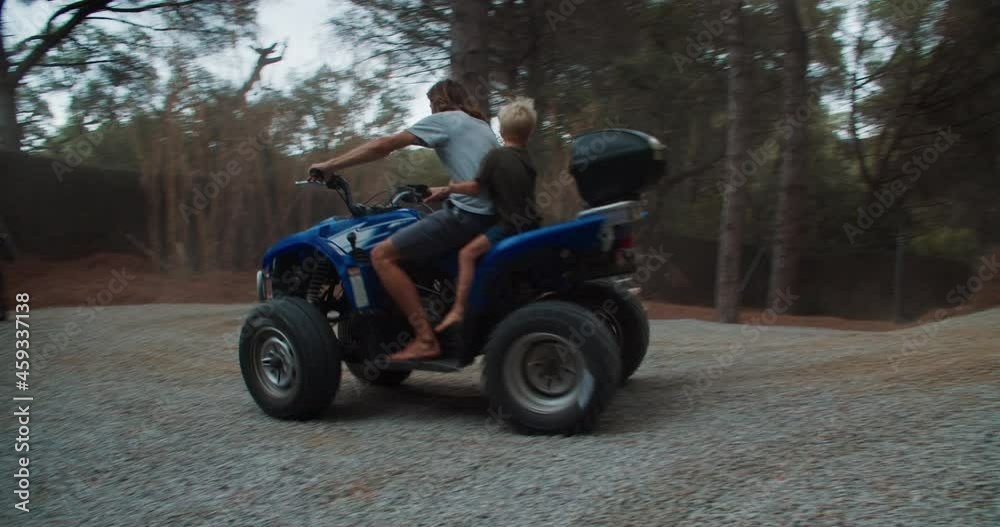 Young men driving fast quad bike with children on the forest and slips around the pine tree during their vacations in rustic house in Catalonia, Spain Young men driving fast quad bike with children on the forest and slips around the pine tree during their vacations in rustic house in Catalonia, Spain